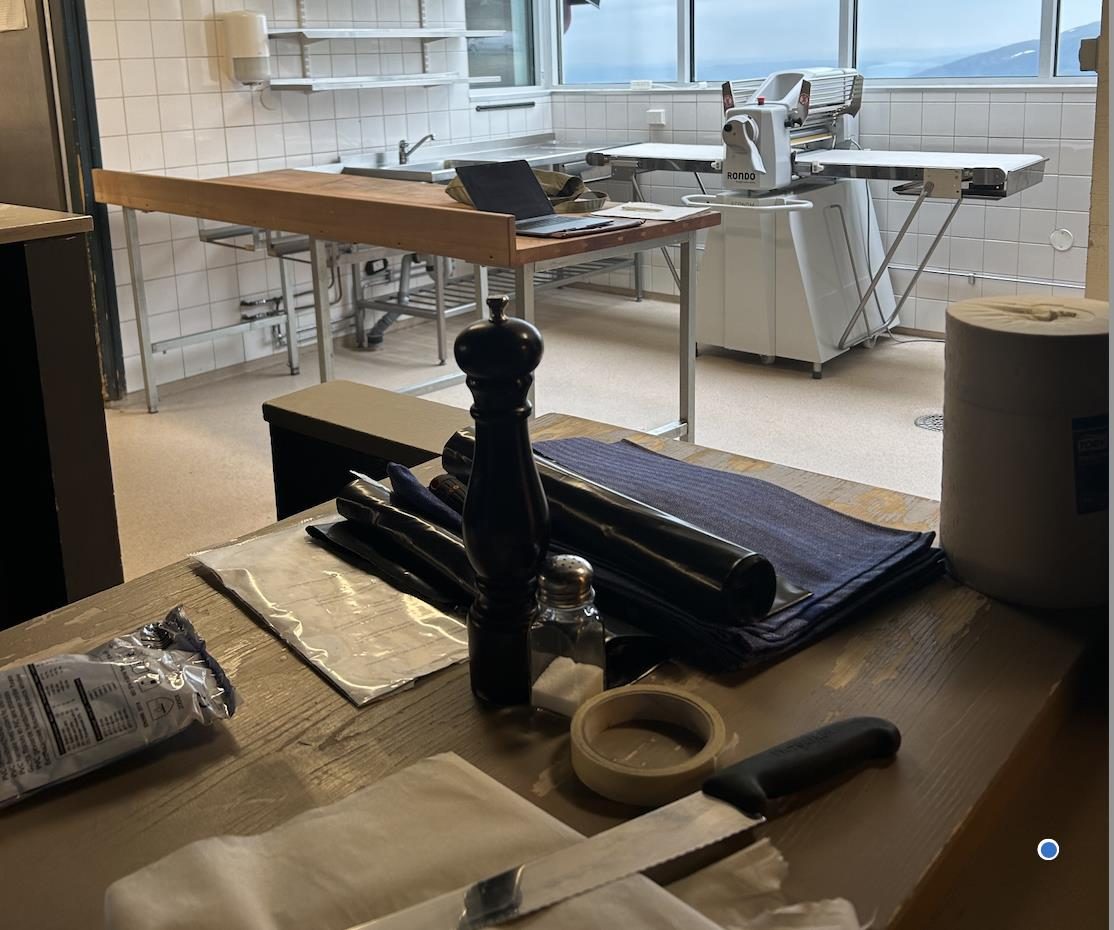Restaurangkök under ombyggnad med rostfria bänkar, bakmaskin och utsikt över fjällandskap genom fönstret.
