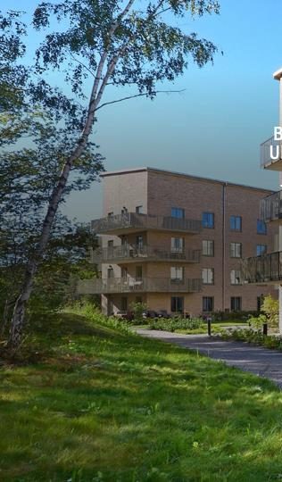 Flerbostadshus i ljust tegel med balkonger, sedd från en grönskande gångväg.